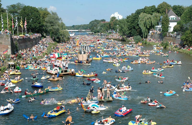 Foto vom „Nabada“: Tausende Menschen baden auf Flößen, Luftmatratzen und kleinen Booten die Donau hinunter. Im Hintergrund die Ulmer Skyline mit dem Ulmer Münster.