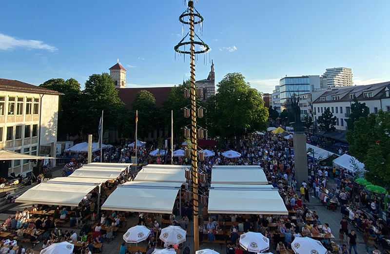 Blick von oben auf den Neu-Ulmer Rathausplatz und die Augsburger Straße mit Biergarnituren, Sonnenschirmen, Essen- und Getränkeständen sowie Fest-Besuchern