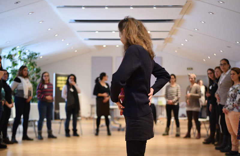 Teilnehmerinnen eines Seminars stehen im Halbkreis um die Leiterin des Seminars.