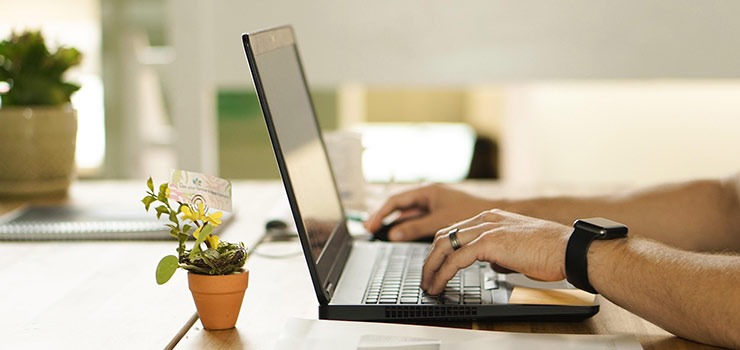 Person tippt auf einem Laptop an einem Schreibtisch