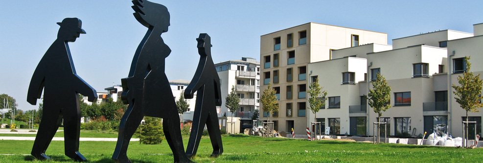 Drei überlebensgroße Skulpturen in Gestalt von Personen, im Hintergrund Wohnhäuser