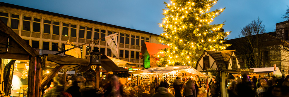 Mittelalterlicher Weihnachtsmarkt mit Marktständen, Besuchern und erleuchtetem Weihnachtsbaum